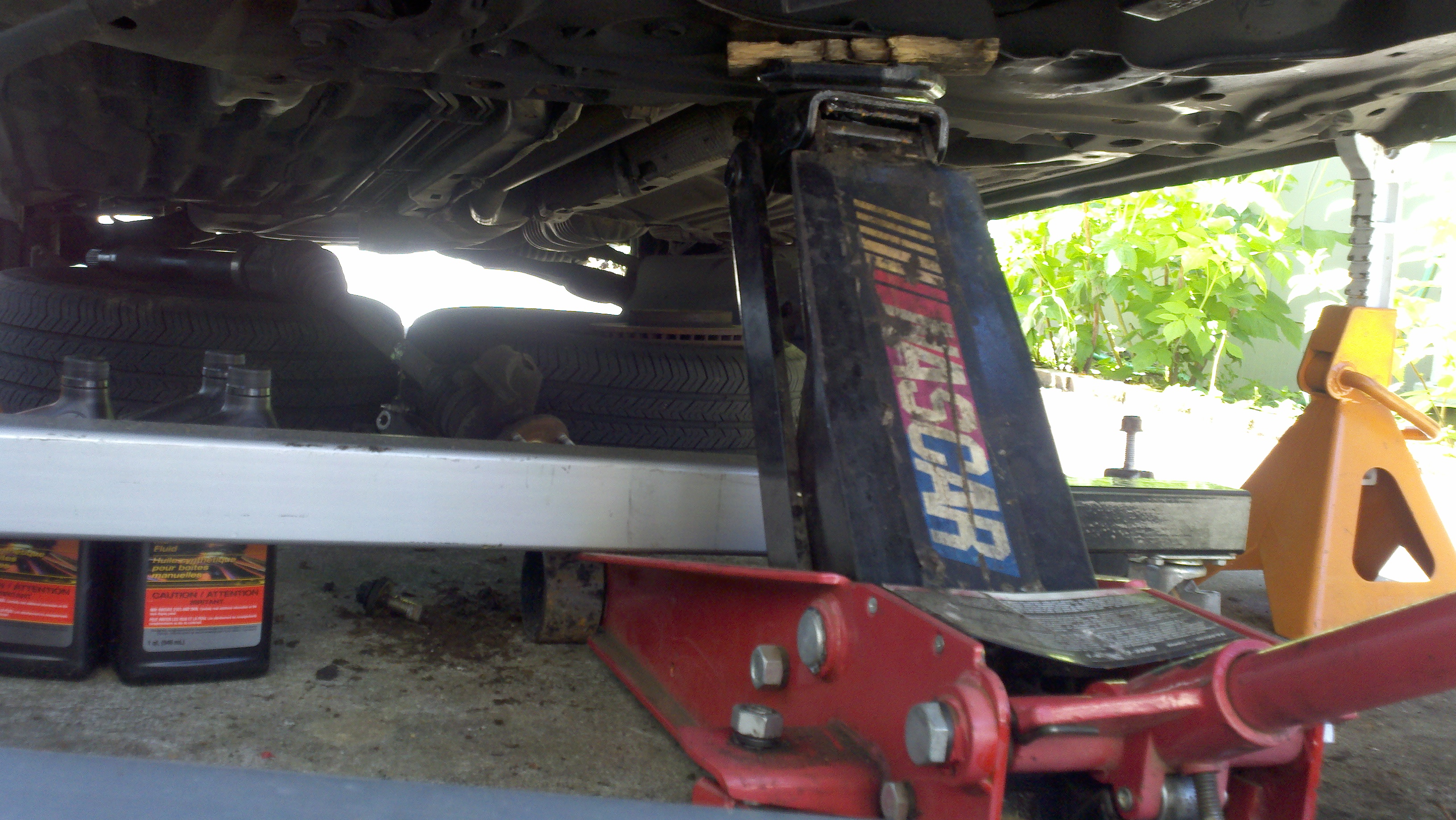 Bottom of my setup, floor jack is in between the legs of the cherry picker and holding up the subframe/crossmember. Bottles of the Ford trans fluid are ...